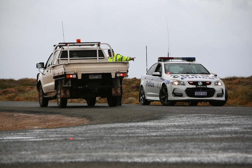A police car and a ute on a quiet country road, with a police officer speaking to the driver of the ute.