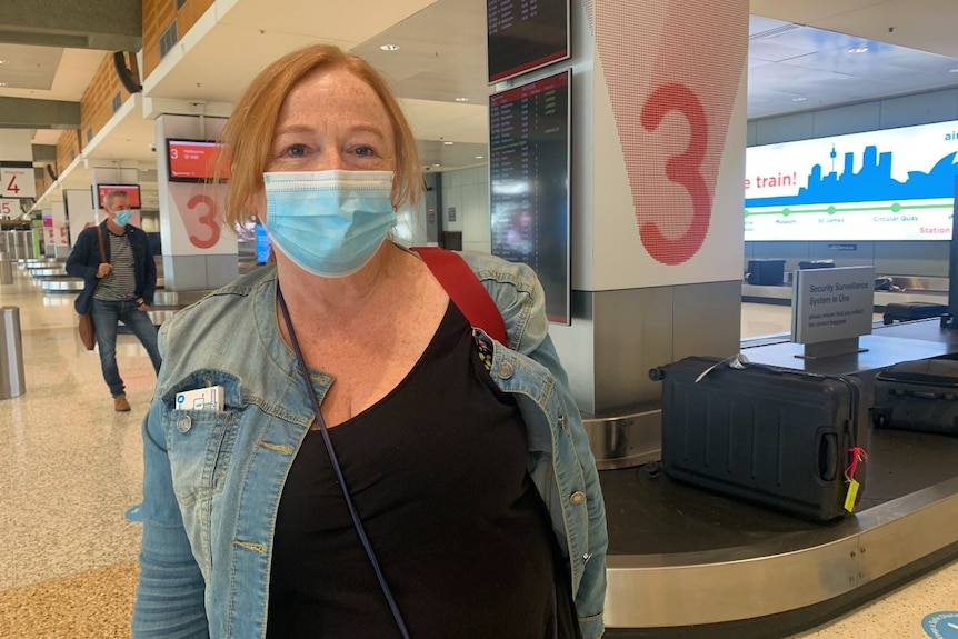 A woman with red hair wearing a mask stands at Sydney Airport.