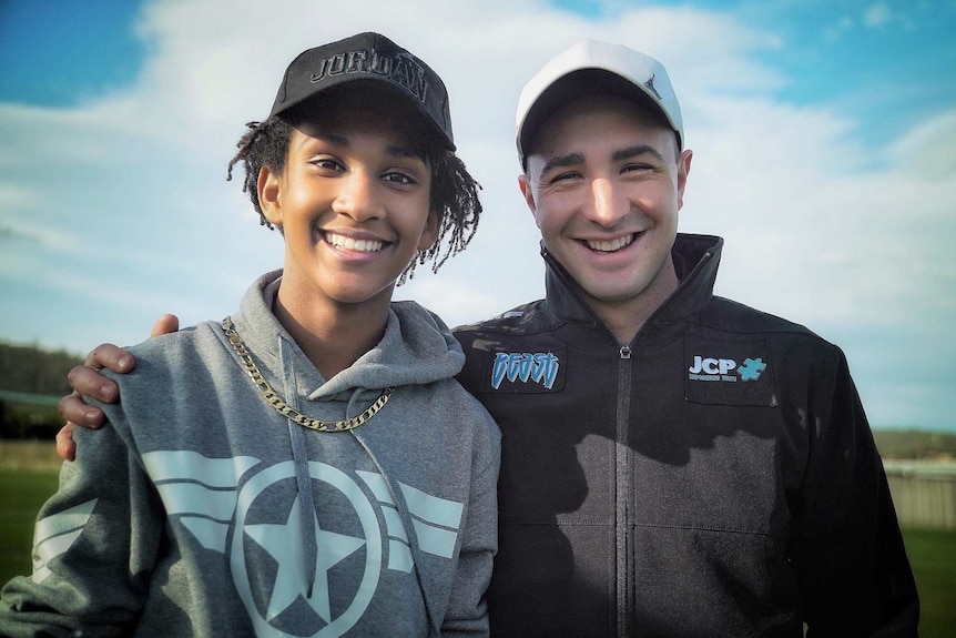 Will Smith and teenager Ahmed Omer smile standing on a soccer field.