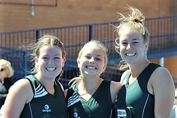 Three sisters stand on a netball court with arms locked around each other.