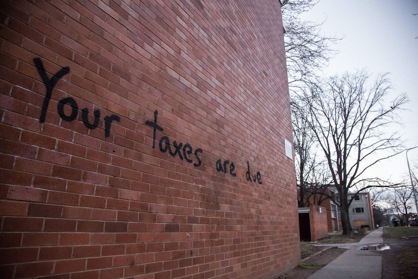 Graffiti on a public housing flat reads 'Your taxes are due'.