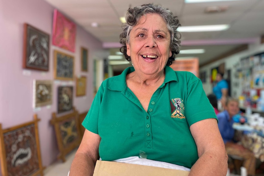 An older indigenous woman in a green shirt holding a box.