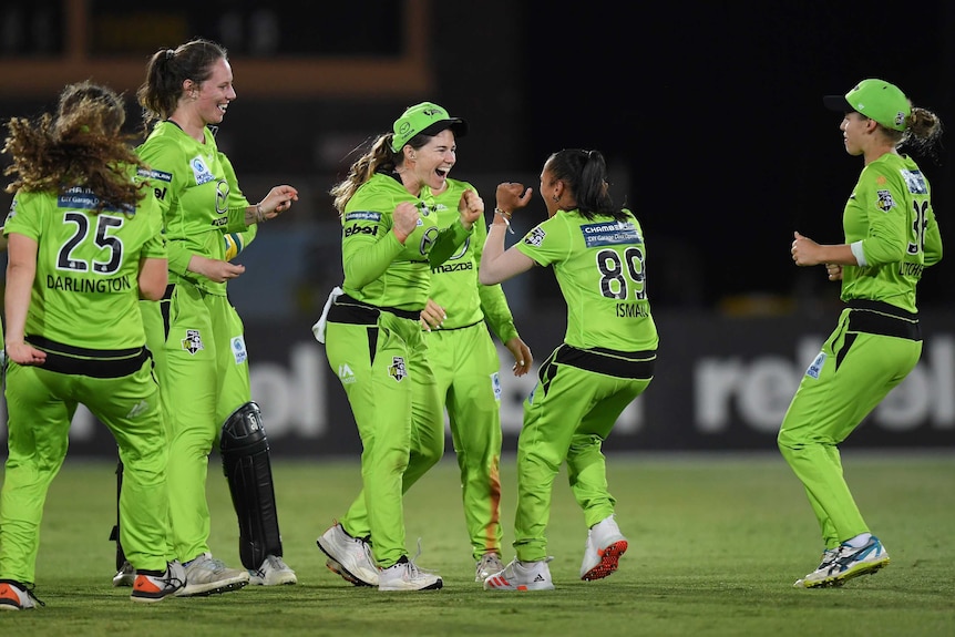 Cricketers wearing fluoro green uniforms celebrate.
