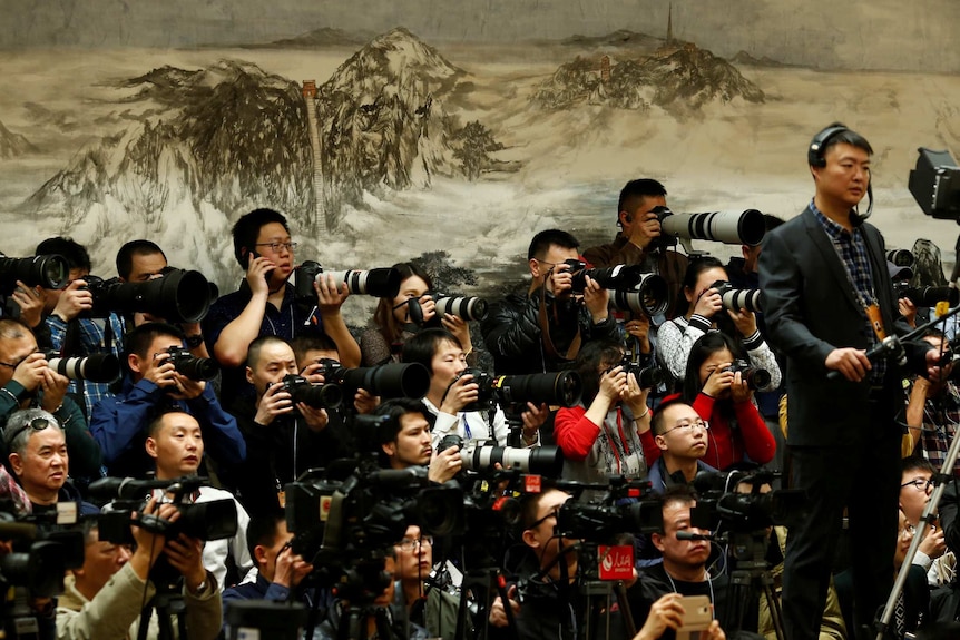 A group of journalists taking photos in front of a mountainous Chinese painting.