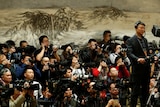 A group of journalists taking photos in front of a mountainous Chinese painting.