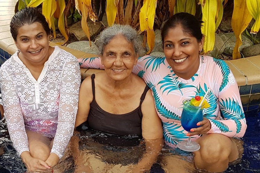 Two younger South Asian women sit alongside an older woman, all in swimsuits and smiling, in jacuzzi