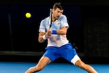 Novak Djokovic slides into a backhand during an Australian Open match against Alex de Minaur.