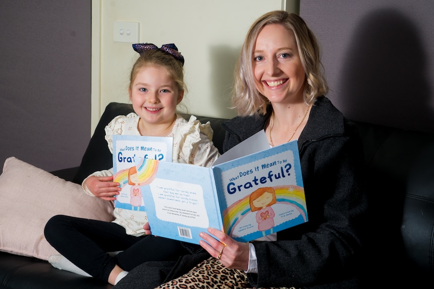 a woman and a girl sit on a couch reading a book together 