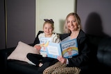 a woman and a girl sit on a couch reading a book together 
