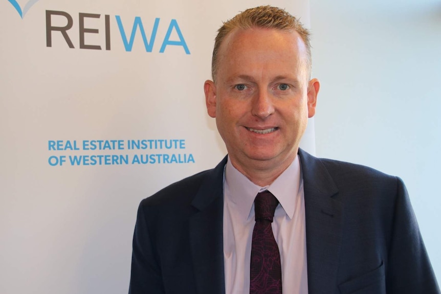 A man stands in front of a REIWA sign.