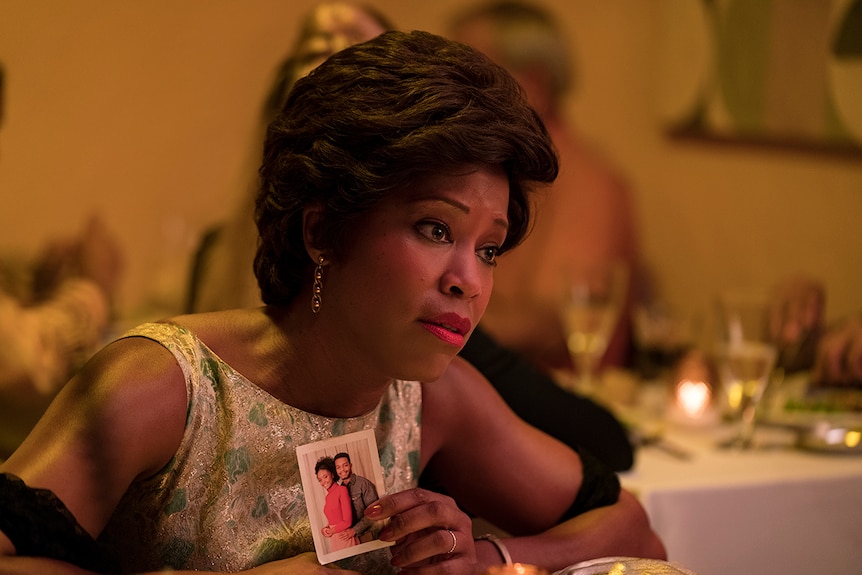 Mid-shot colour still of Regina King sitting at dining table holding photograph in 2018 film If Beale Street Could Talk.