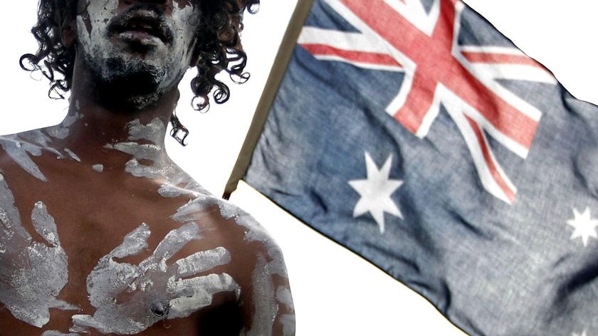 An Aboriginal performer stands in front of an Australian flag