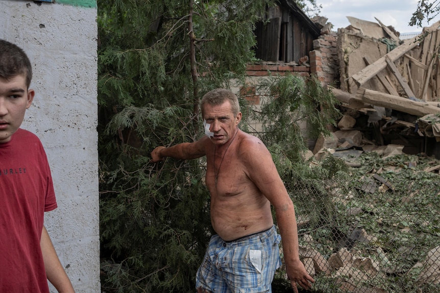 Injured Ukrainian residents stand in front of destroyed houses.