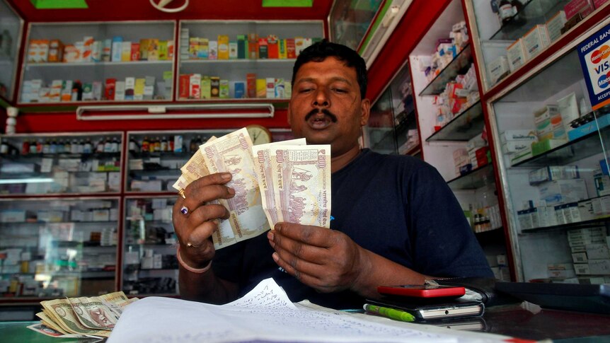 A shopkeeper counts 500 Indian rupee banknotes at a cash counter inside a medicine shop in Agartala.