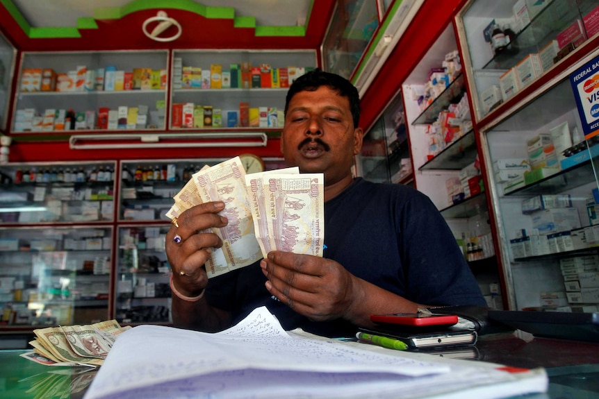 A shopkeeper counts 500 Indian rupee banknotes at a cash counter inside a medicine shop in Agartala.