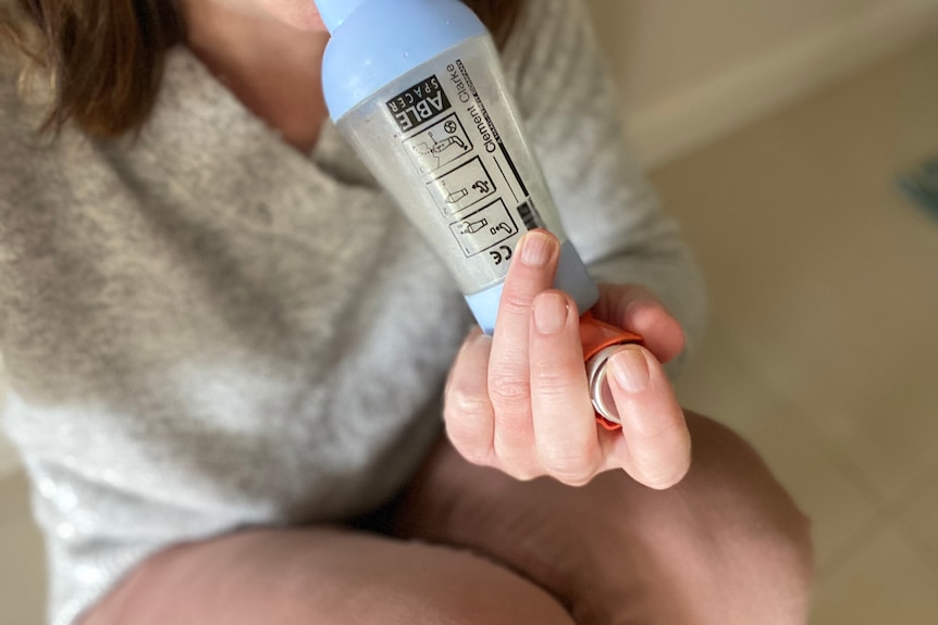 Woman using an asthma reliever through spacer, sitting on ground