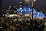 A large crowd outside Flinders Street Station which was lit up in blue lights.