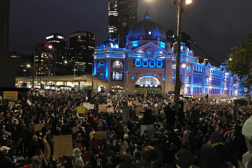 A large crowd outside Flinders Street Station which was lit up in blue lights.