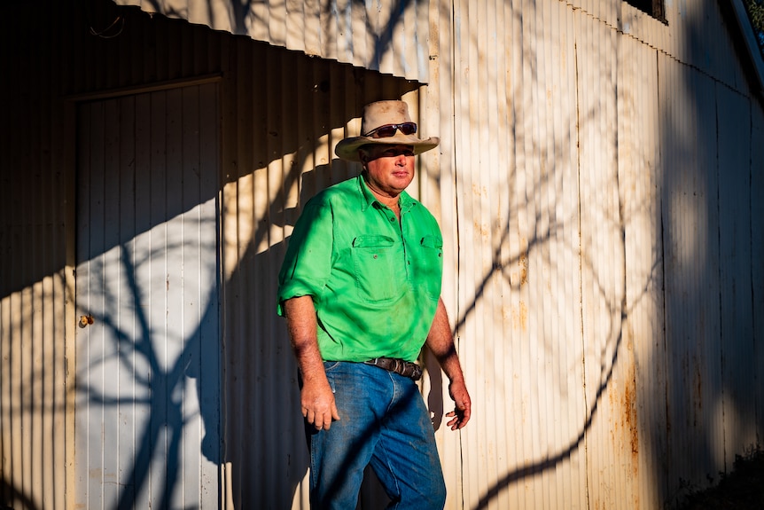 Boyd Webb standing in front of a shed with corrugated iron walls, under jagged shadows from a tree.