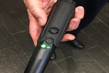 A person holds a black sick-like device with green lights on it
