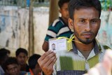 A Rohingya man holds up a freshly printed card that features his headshot.