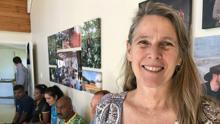 Molly Harriss Olson smiles with people and photos of coffee plantations in the background.