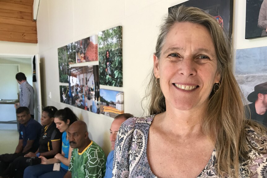 Molly Harriss Olson smiles with people and photos of coffee plantations in the background.