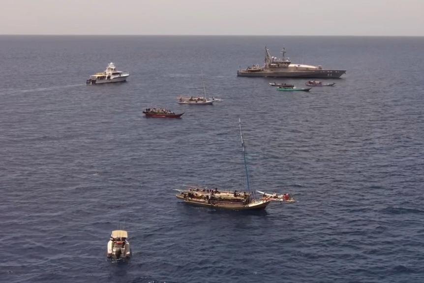 un grand patrouilleur et plusieurs petits bateaux de pêche entourés par la mer