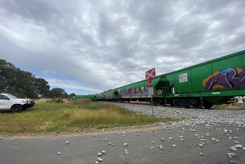 Derailed train carriages on a line, with rocks scattered over a level crossing with a road.
