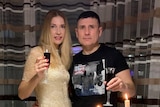A woman with long, blonde hair and a man with dark hair wearing a black T-shirt. Both are toasting the new year.