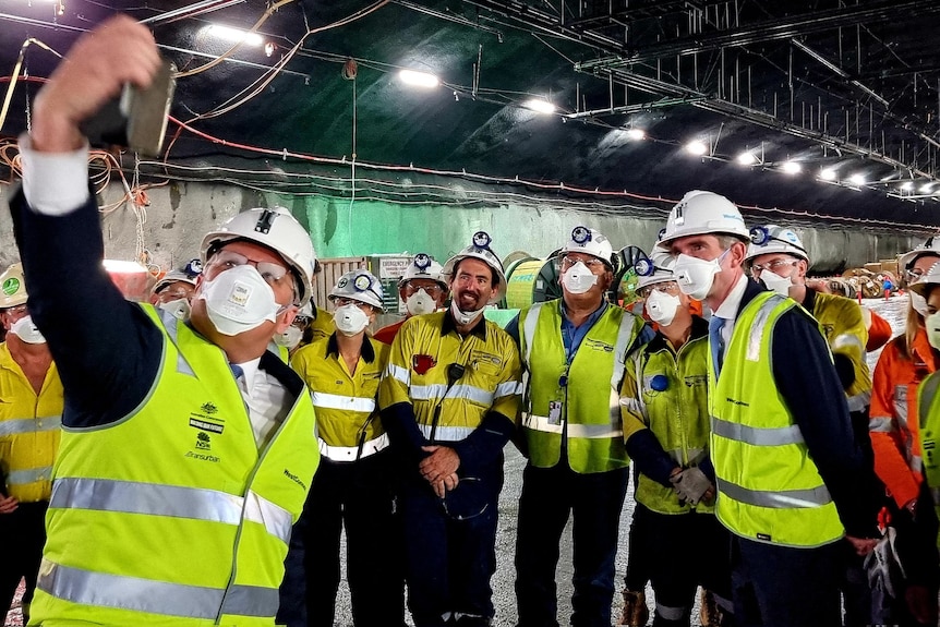 The Prime Minister holds a phone up to take a selfie with workers in high-visibility vests while inside a tunnel.