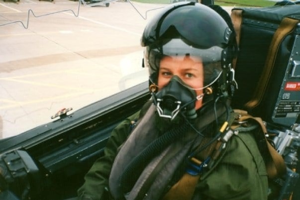 A woman sits in the cockpit of a military plane.