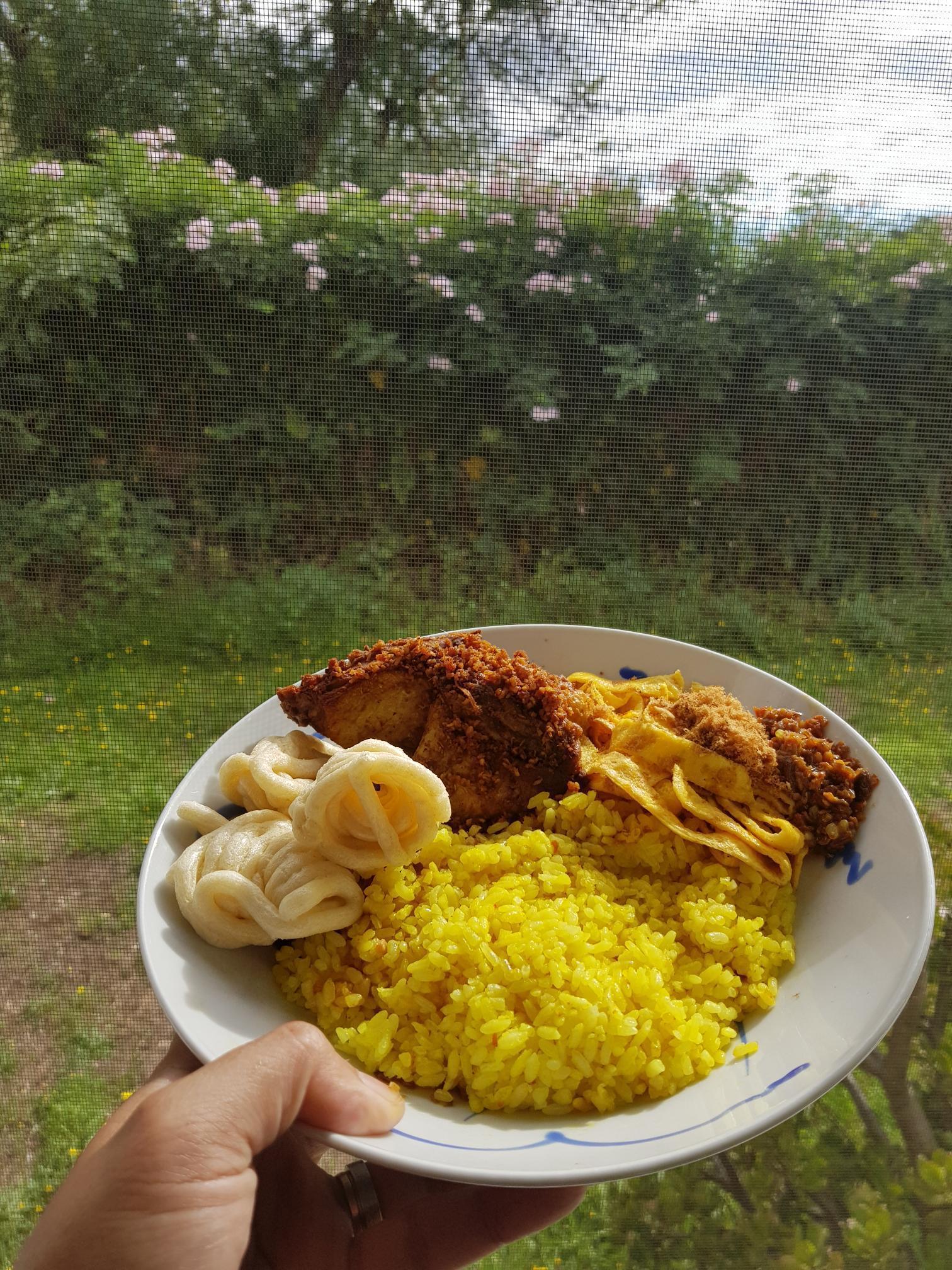 A plate of yellow rice with chicken, egg, and cracker