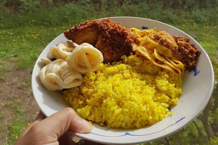 A plate of yellow rice with chicken, egg, and cracker