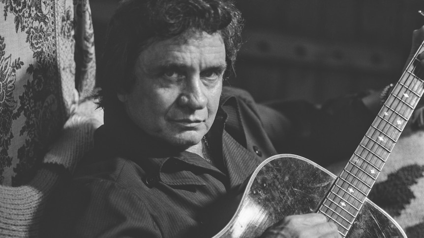 Black and white photo of Johnny Cash looking into the camera while playing an acoustic guitar