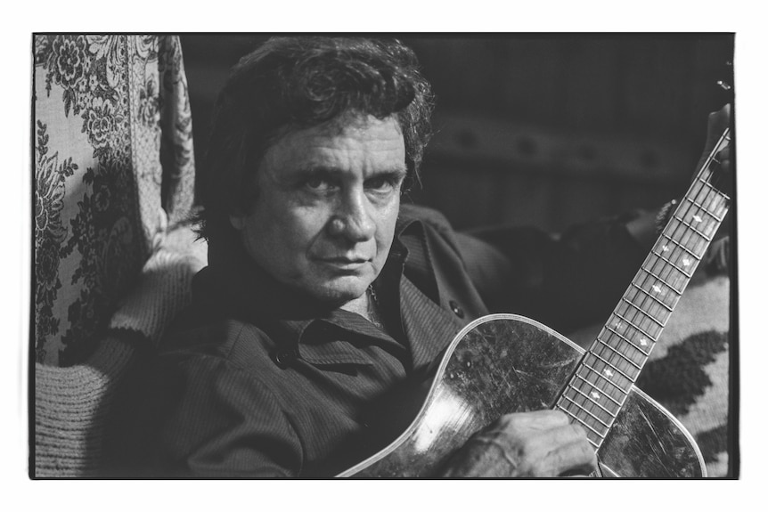 Black and white photo of Johnny Cash looking into the camera while playing an acoustic guitar
