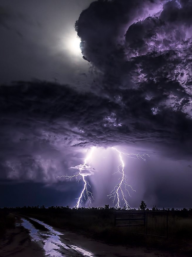 Two bolts of lightning emerging from a cloudy sky, wet gravel road in front