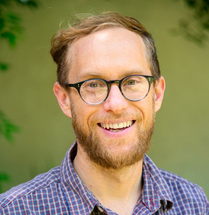 A man wearing glasses smiling into the camera with a green background