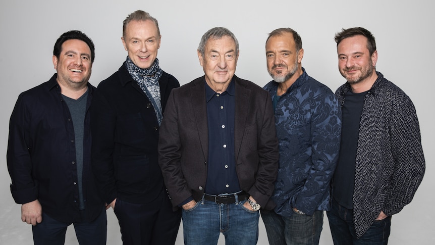 5 smiling men standing together against a grey background