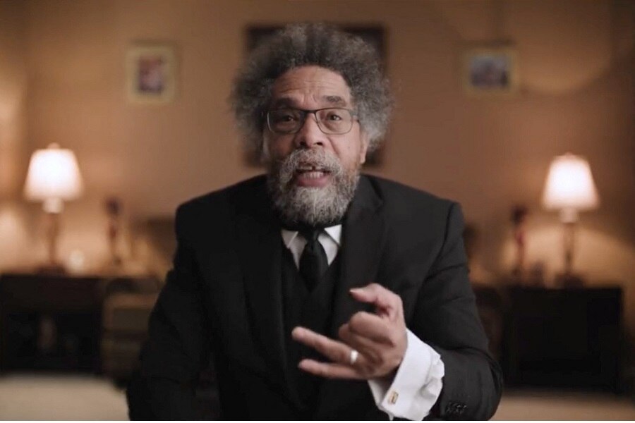 An older black man with a beard and grey frizzy hair gestures as he speaks to the camera in a tastefully lit room.