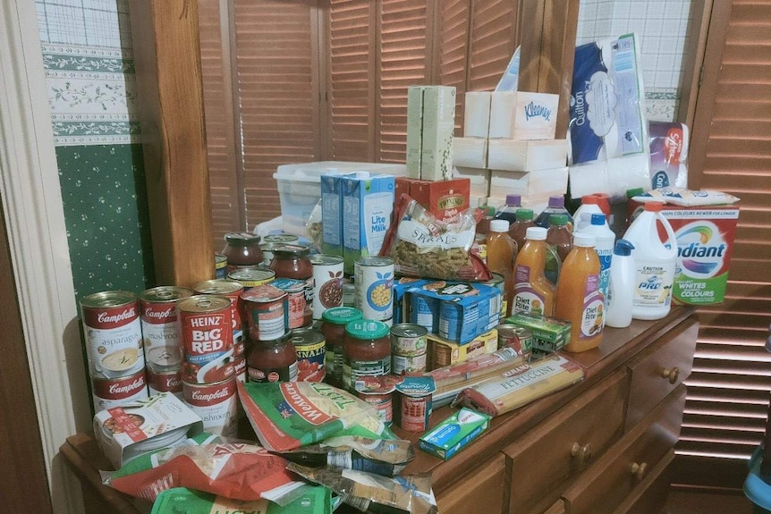 A pile of groceries stacked up on a set of drawers.