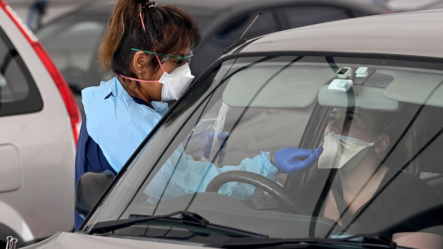 a healthcare worker conducting a swab to a person in a car