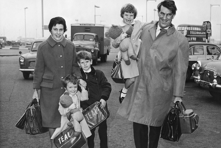 A family of five hold bags in an airport carpark in a 1960s black and while photo.