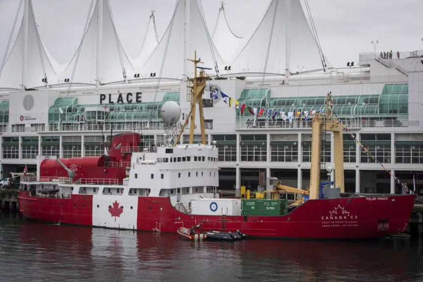 A red and white ship displaying Canada's flag on the hull on the water.