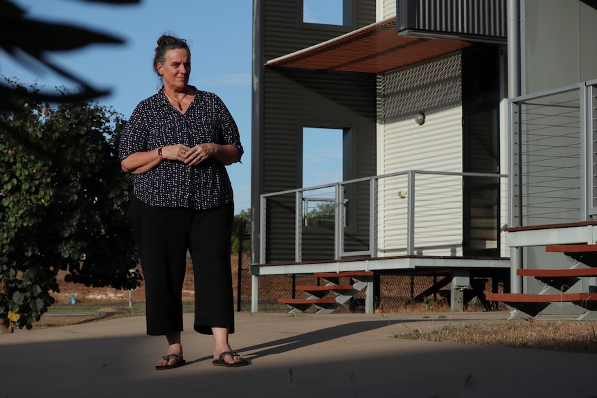 A woman stands in front of an empty house in a suburban street.
