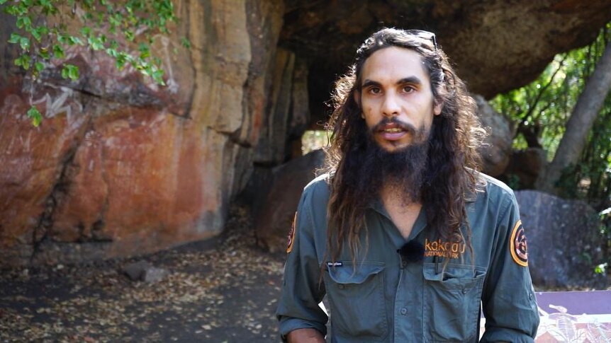 Aboriginal man stands in front of rock formation