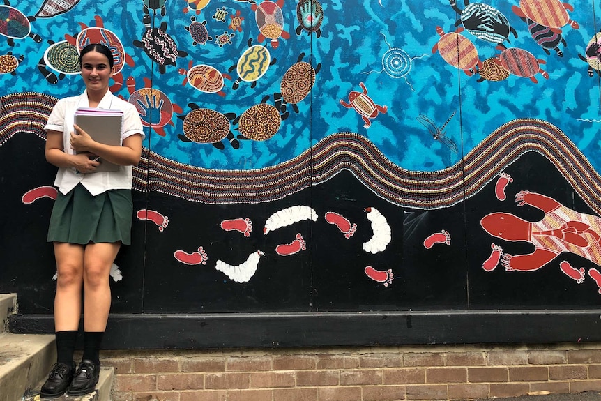 Amta Audesh standing against a mural