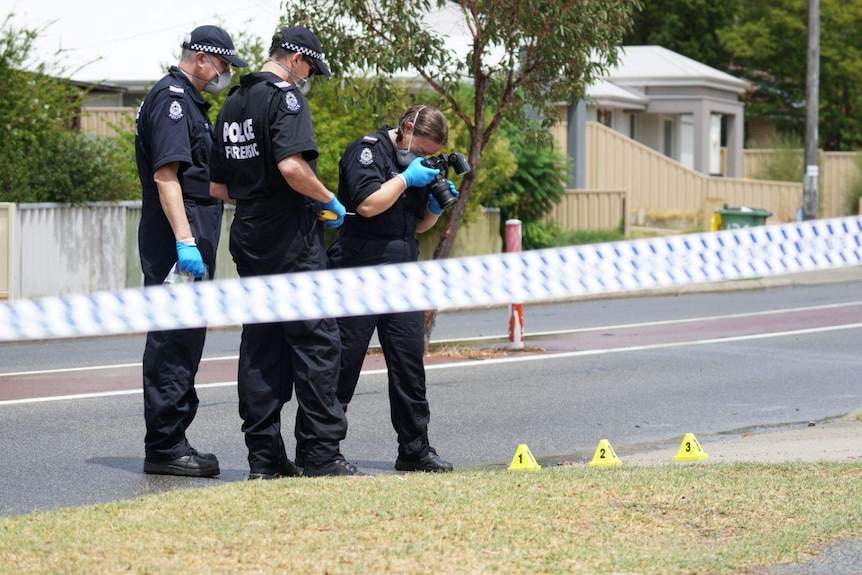 A forensic officer takes a photo of the road, while two others look on, behind police tape.