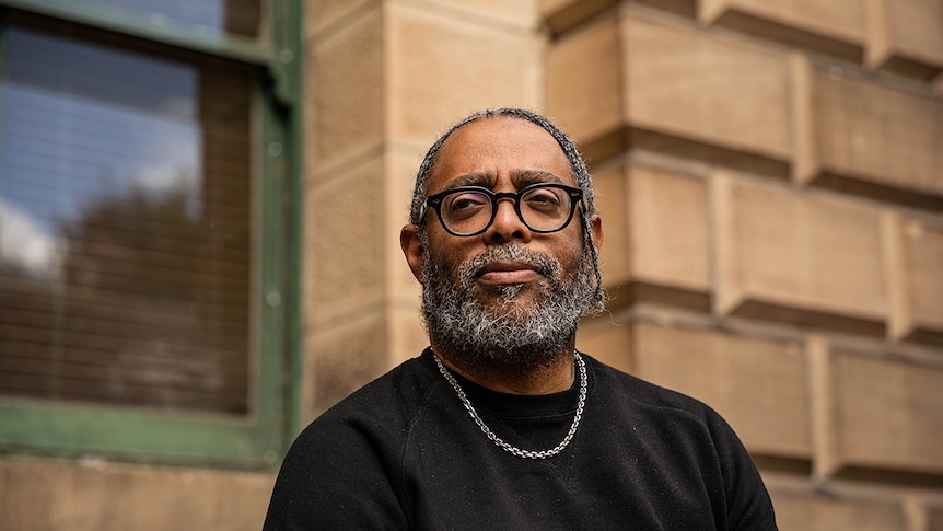 Colour close-up photo of artist Arthur Jafa posing in front of sandstone building at the National Art School in Sydney.