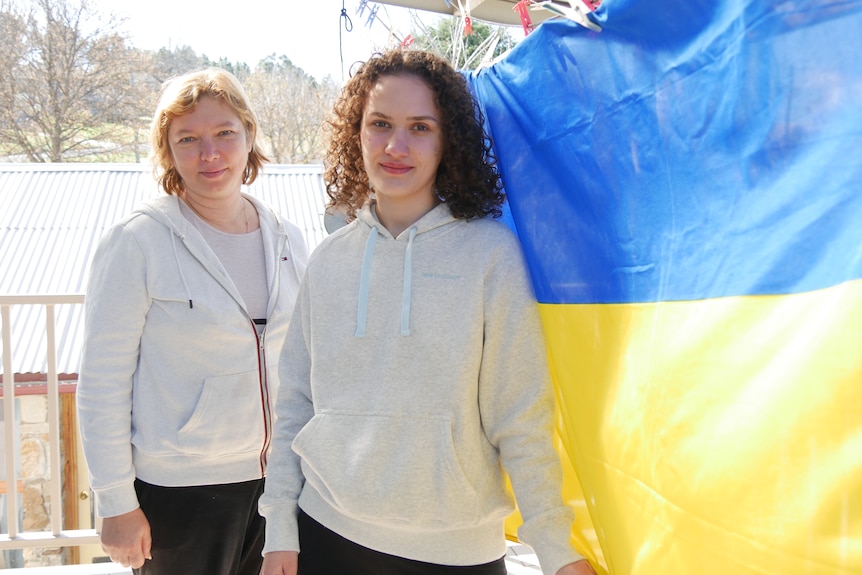 Two women stand next to a Ukrainian flag